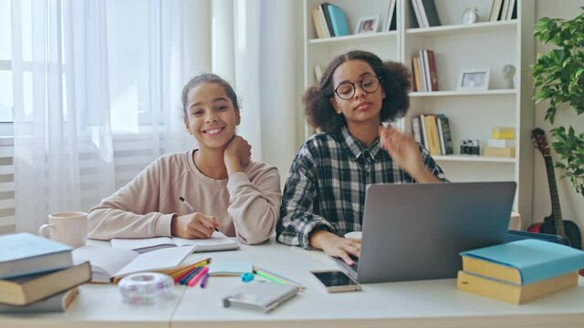 Two schoolgirl smiling at camera, learning foreign language at home, internet