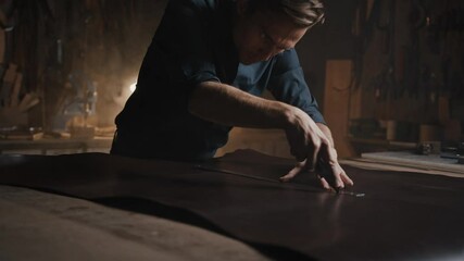Shoe making process. Cinematic shot of concentrated professional young man tailor cutting piece of leather at workshop - Powered by Adobe