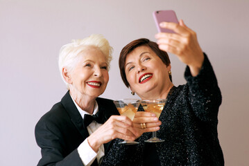 Two beautiful stylish mature senior women drinking wine and making selfie photo. Fun, party, technology, style, celebration concept