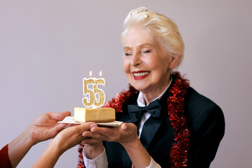 senior stylish woman in tuxedo blowing candle fifty five on her birthday cake. Lifestyle, positive,...