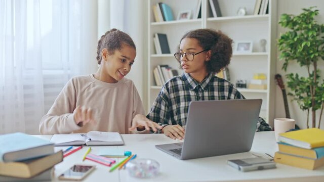 African american teenager helping best friend to do online homework on laptop