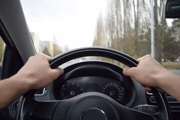Male hands firmly hold the steering wheel of the car