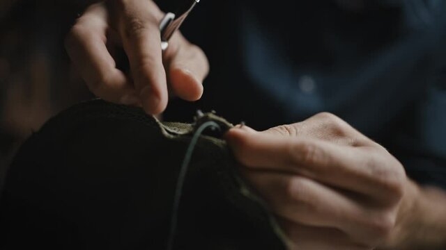 Unrecognizable man craftsman unpicking old product for reuse, cutting seam with knife, close up of hands, tracking shot