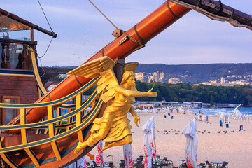View of the bow and the figurehead of a stylized vintage sailboat close-up against the backdrop of the beaches of Varna, on the Black Sea coast of Bulgaria - obrazy, fototapety, plakaty