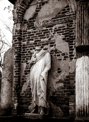 black and white photo. a statue without a head. a statue against a brick wall. destroyed building