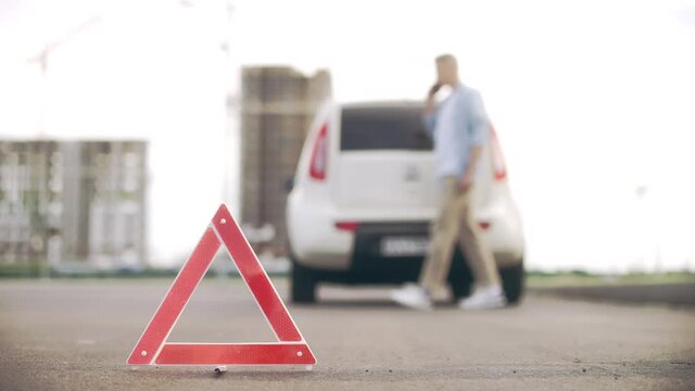 Nervous driver calling car service or tow truck, warning triangle stands on road