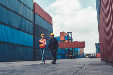 Industrial worker works with co-worker at overseas shipping container yard . Logistics supply chain management and international goods export concept . - obrazy, fototapety, plakaty