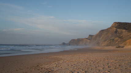Praia da Cordoama in Portugal. Golden surfing coastline. Fog on the rock seashore. Golden empty coast in evening