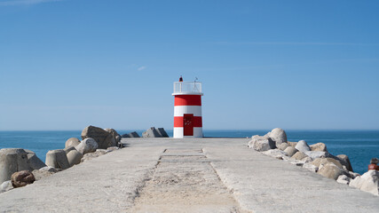 White red lighthouse on a stone pier in Nazare. A red and white short lighthouse
