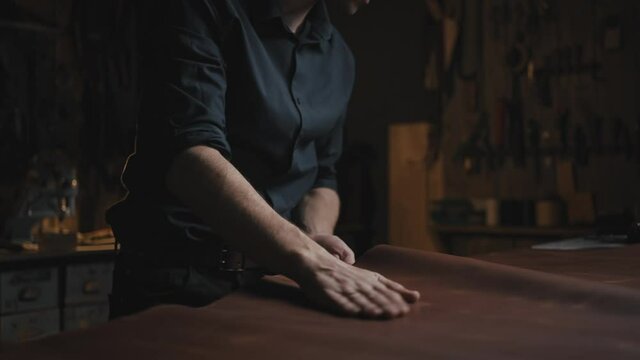 Designing and tailoring clothes. Professional male tailor testing and smoothing leather before work with it at workshop