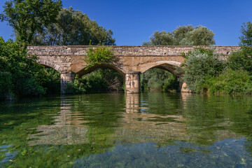 Fototapeta na wymiar An old stone bridge on the green clear river Zrmanja in Croatia