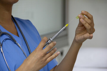 Close-up of a doctor's hands holding a syringe. Portrait without face with stethoscope and light blue uniform.