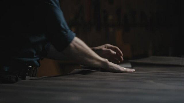 Tailor workshop. Close up of unrecognizable male craftsman rolling out and smoothing piece of leather on table