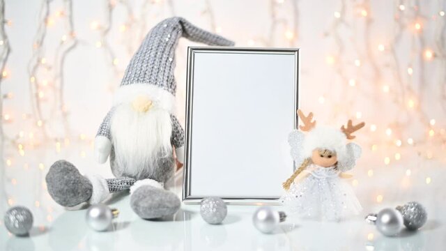 Cute silver Christmas arrangement of  gnome, angel and little ornaments on the table around silver empty frame. 