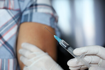 Vaccination during covid-19 pandemic, female hand in protective glove with syringe. Nurse preparing to injection into a male shoulder