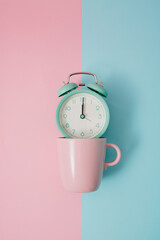 Minimalist concept idea light blue alarm clock in pink coffee mug with vintage color background on pop art style