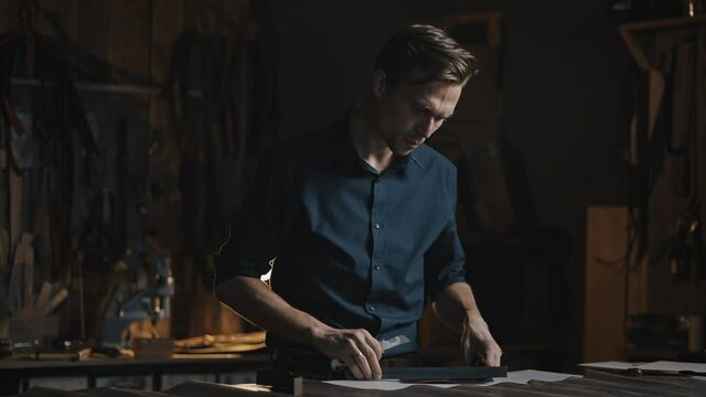 Professional male tailor cutting leather in pieces, preparing material for sewing production, working at workshop