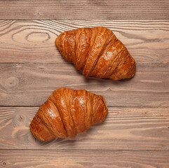 Two French croissants on a brown wooden background.