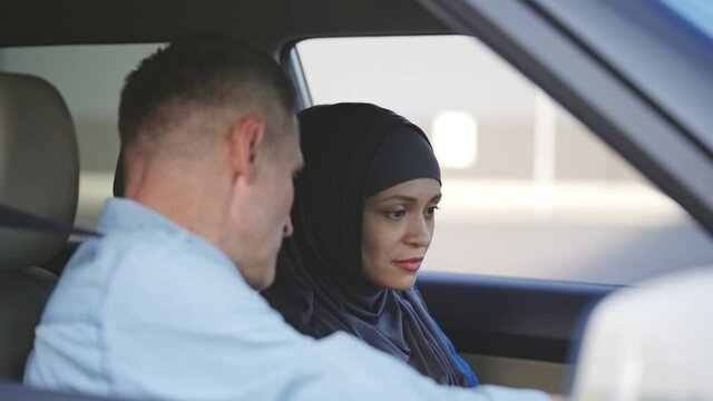 Driving instructor explaining dashboard to middle-eastern woman, driving lesson