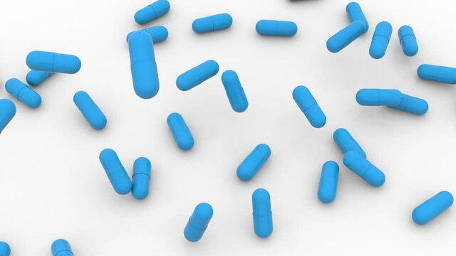 The camera looks from above as blue hard gelatin capsules fall onto a white surface. Molnupiravir.