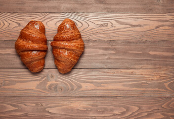 Two French croissants close-up on a brown wooden background.