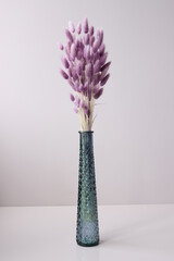 Glass vase with purple dried flowers standing on table background