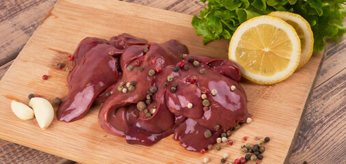 Raw chicken liver on a wooden board, beautifully served with pepper, lemon and herbs