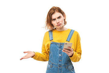 Pensive thinking redhead girl holding smartphone with upset face in yellow clothes isolated on white studio background