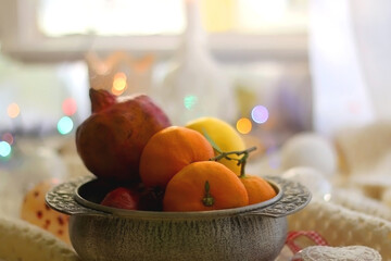 Silver bowl with various fruit, soft blanket and various Christmas decorations. Hygge at home. Selective focus.