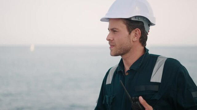 Young handsome man port worker with walkie-talkie in hand controlling work process in shipping port