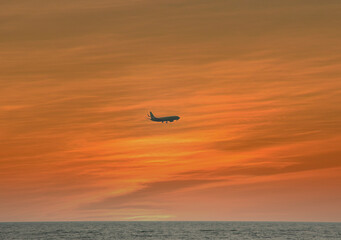 the silhouette of an airplane against the background of the evening orange sky, the sun has set over the horizon and the sea below.