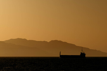 Fototapeta premium Cargo Ship at Sunset with Island in Background