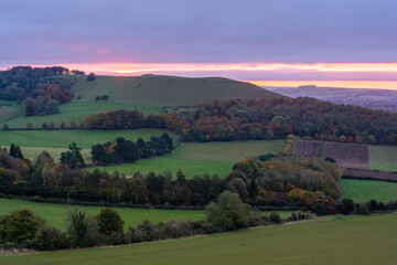 Fototapeta na wymiar dramatic purple, red, pink and orange sky as the sun rises over Giant's Grave, Oare. View from South facing edge of the Marlborough Downs, Pewsey Vale, Wiltshire AONB 