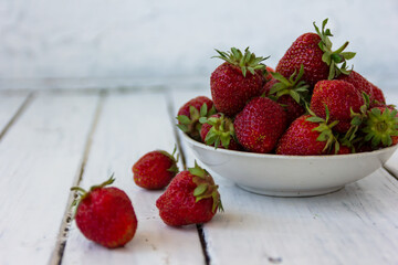 Ripe red strawberries lie in a white cup on a wooden white table. Copy space