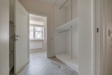 rows of shelves and clothes hangers in empty big wardrobe room in modern apartment or hotel