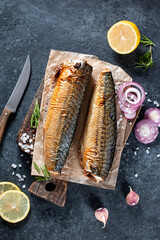 Delicious smoked fish mackerel on paper with garlic and onion. On rustic background