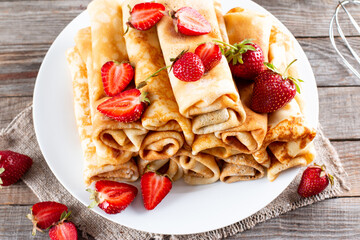 Many pancakes with strawberries. Maslenitsa. A stack of thin freshly baked pancakes with strawberry berries on a wooden background.