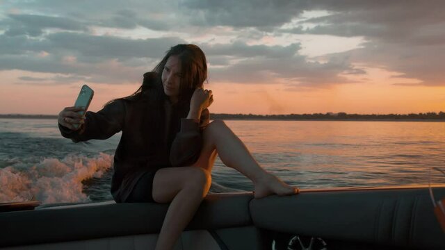 A woman takes a picture of herself at sunset in a motor boat
