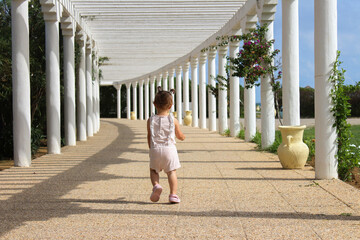 Little girl runs along the alley with white columns in summer.