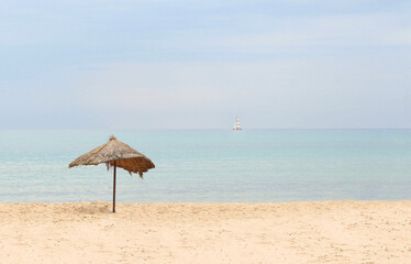 Straw beach umbrella on a tropical sandy beach on a background of blue sea on a sunny day.