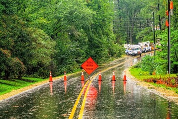 An emergency storm roadblock on a rural road with orange cones and utility trucks in the background.