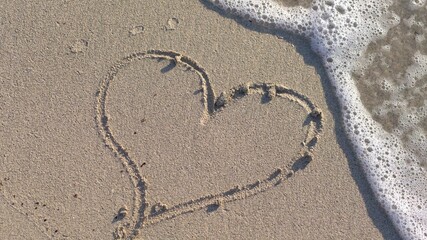 Woman Drawing a Heart on the Sand at Sunset