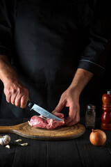 Chef cuts meat with a knife in the kitchen prepares food. Vegetables and spices on a table in a restaurant for preparing a delicious lunch