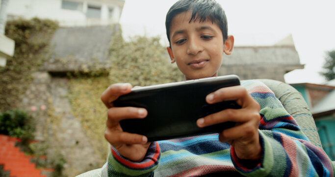 Joyful kid drom India playing with a smartphone outdoors on a sunny day