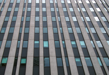 close up perspective detail of tall high rise brutalist style office building with white vertical concrete lines and dark windows