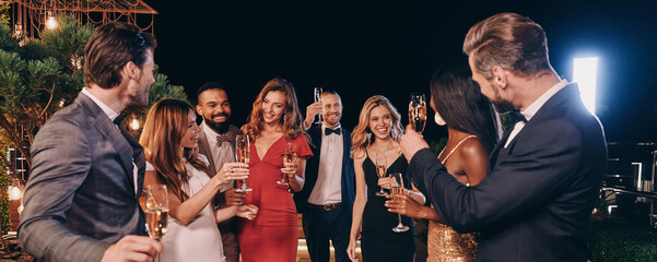 Group of beautiful people in formalwear communicating and smiling while spending time on luxury...