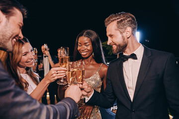 Group of beautiful people in formalwear toasting with champagne and smiling while spending time on...