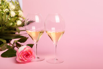 Romantic lovely holiday card with flowers and 2 glasses of italian white wine on pink background. Romantic atmosphere for people in love. Beautiful wedding day postcard.