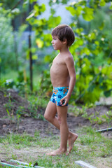 Kid's outdoor activity. Smile toddler boy wearing a blue swimming shorts running and playing with water splashes having fun in a backyard on a sunny hot summer day. Caucasian boy plays hide and seek