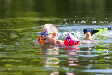 Cute boy is swimming in the small river with his armbands and goggles